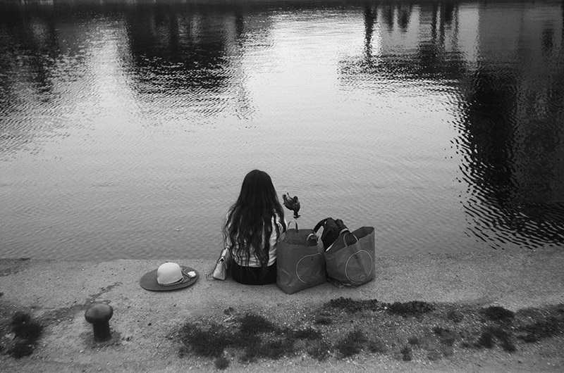 A woman sat by the a canal with some shopping